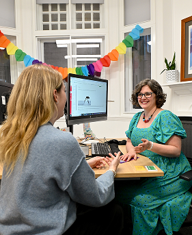 A women with brown hair and wearing a green dress, talking to a student with blo